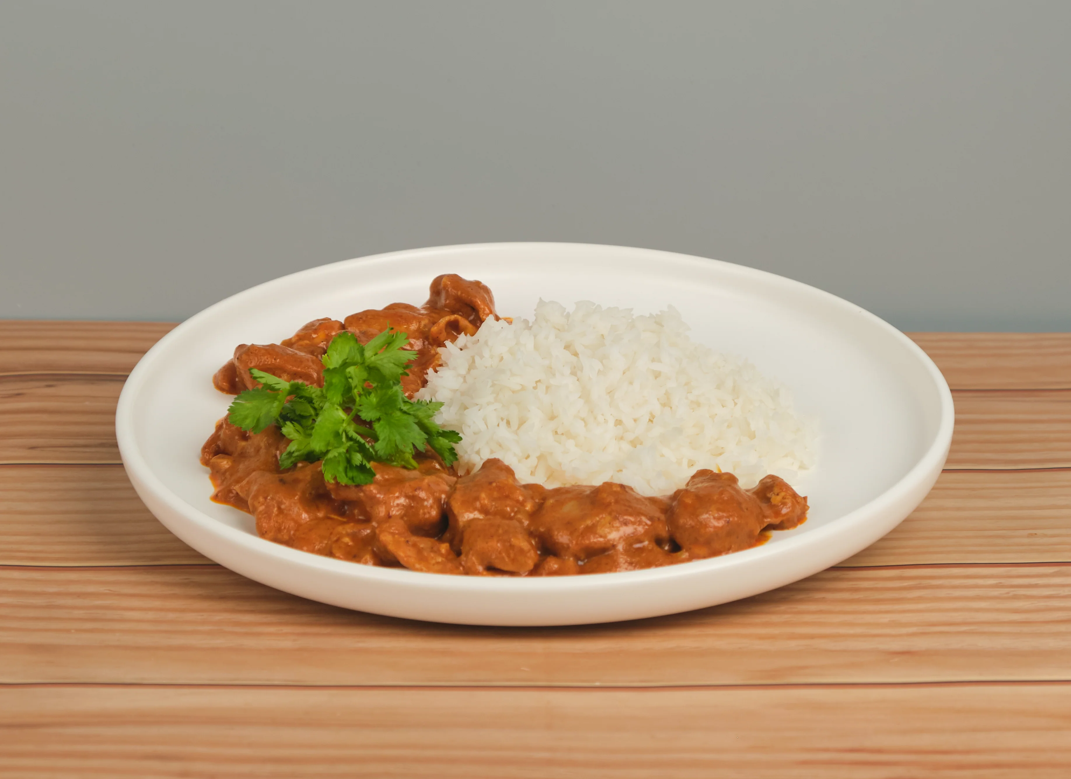 Buttered chicken plated for service, rich orange-red sauce over steamed rice